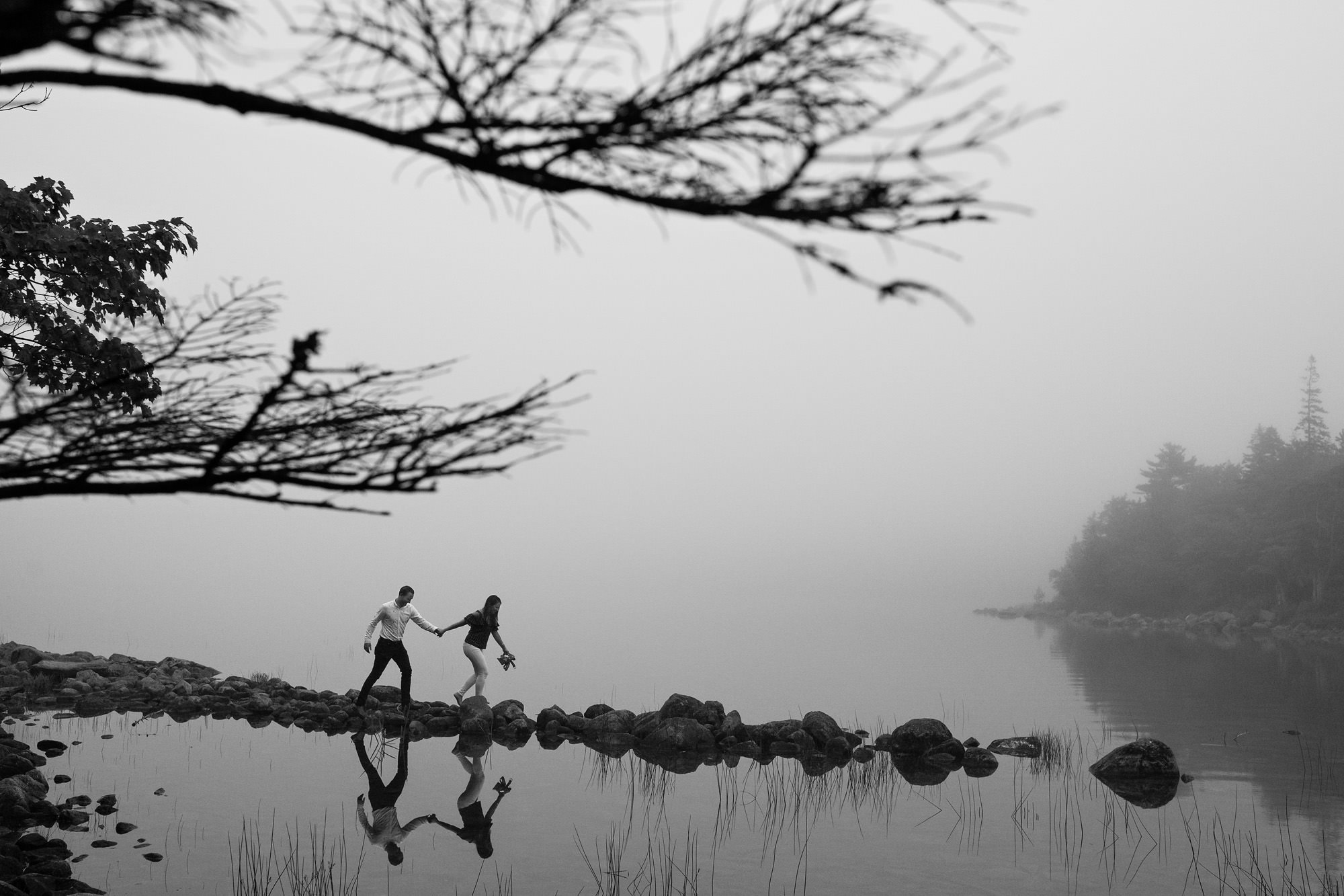 A couple takes engagement portraits around Jordan Pond in Acadia on a foggy evening.