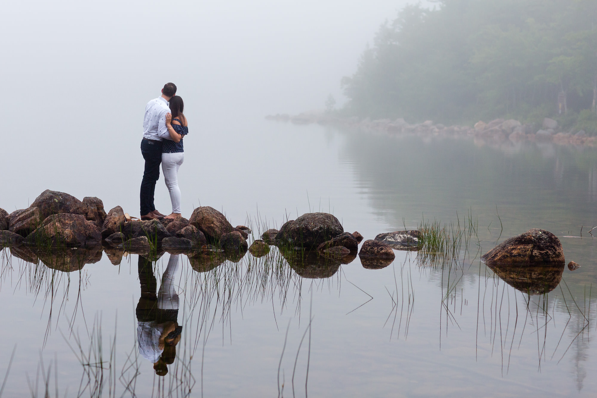 A couple takes engagement portraits around Jordan Pond in Acadia on a foggy evening.
