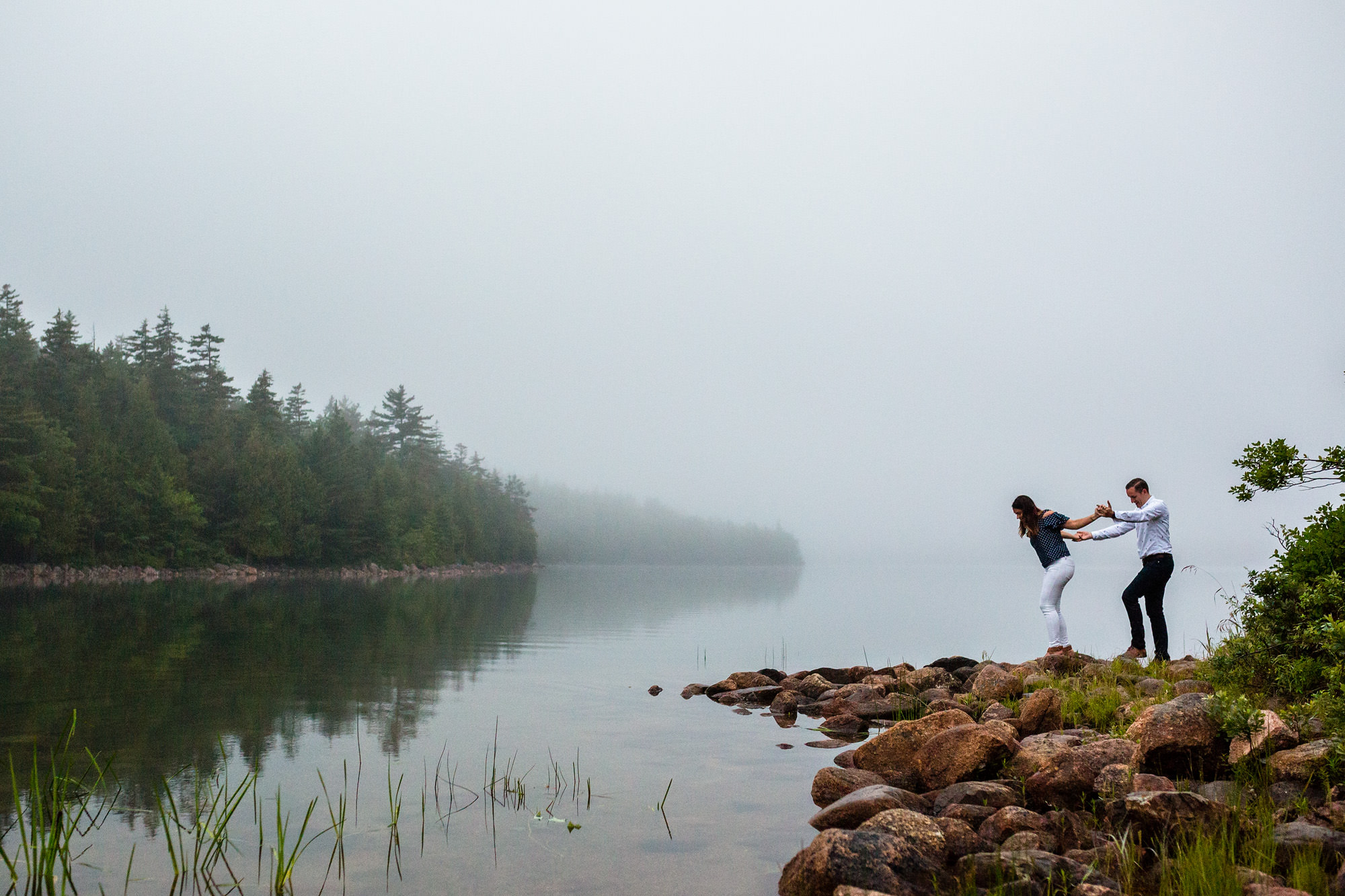 A couple takes engagement portraits around Jordan Pond in Acadia on a foggy evening.