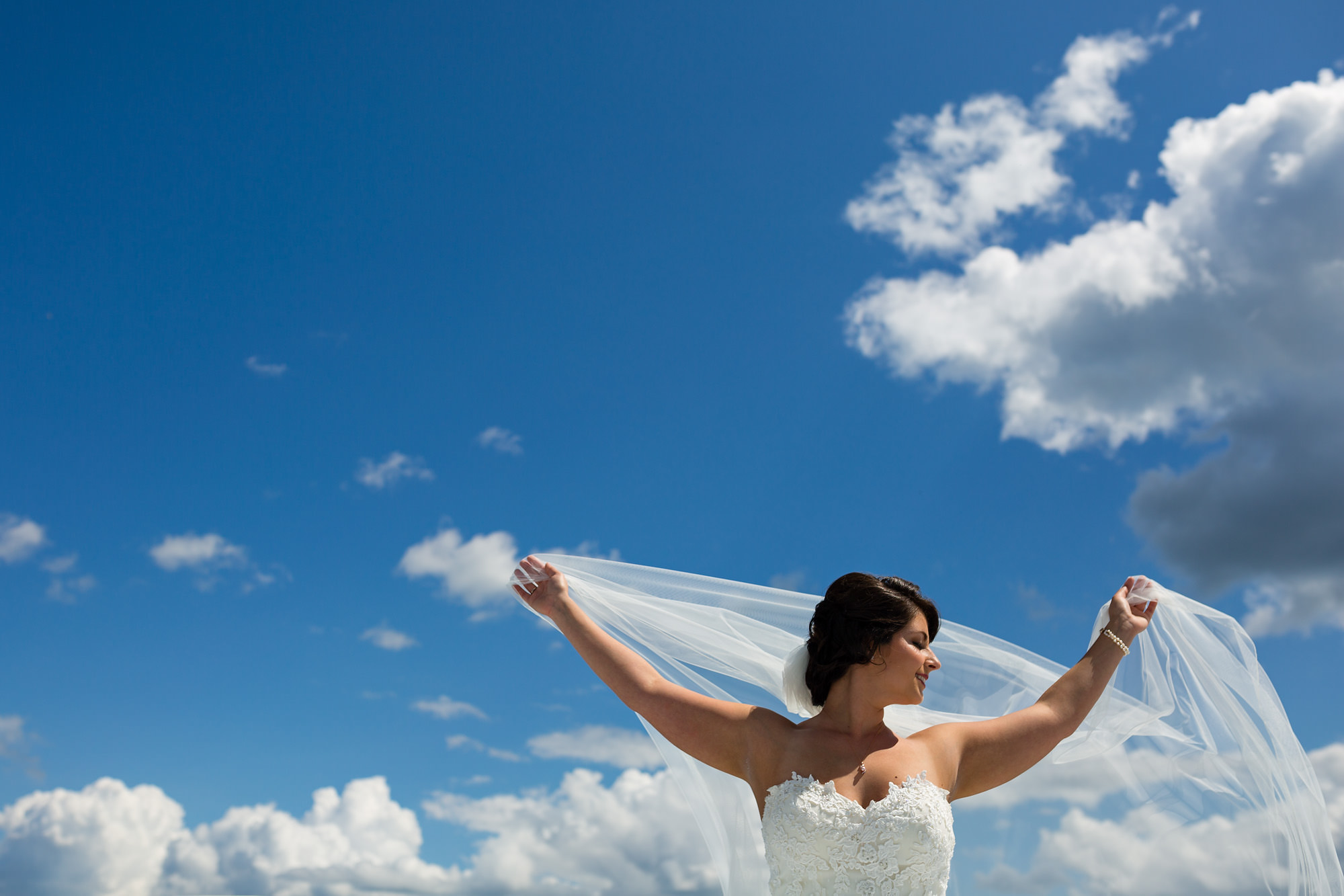 A bride poses against the sky at her wedding at French's Point