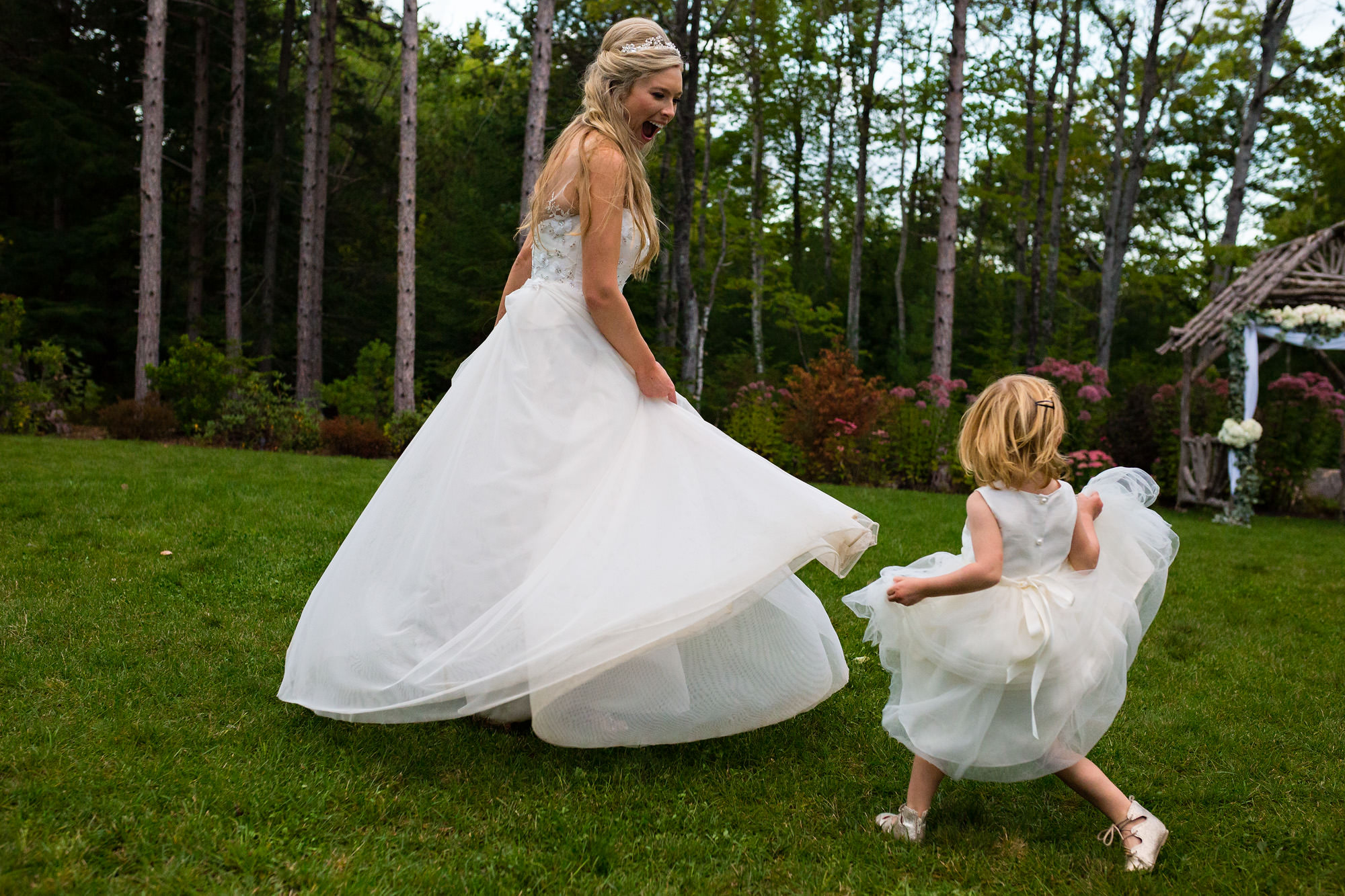 A bride and flower girl share a twirling challenge at a Maine wedding.
