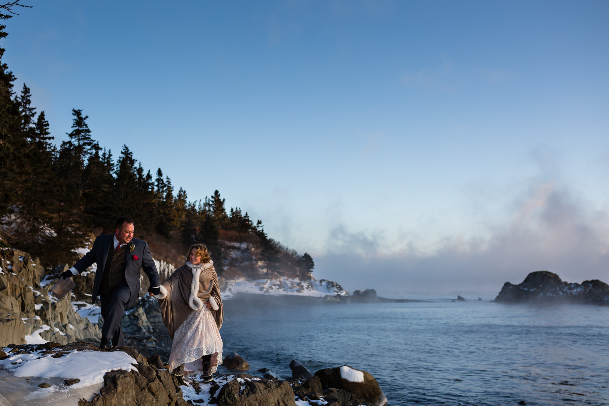 A bride and groom take photos featuring sea smoke during their winter elopement in Lubec, Maine