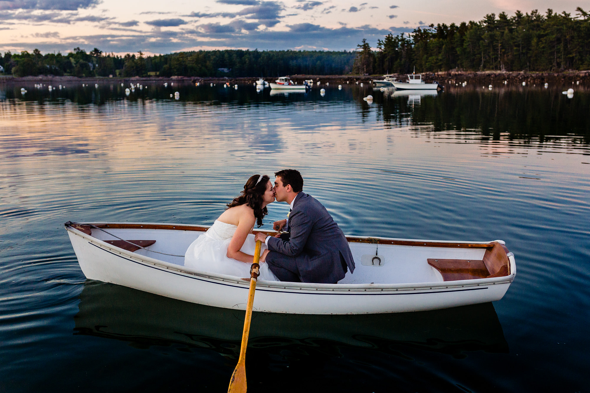 A bride and groom row in a rowboat at sunset at their coastal Maine wedding
