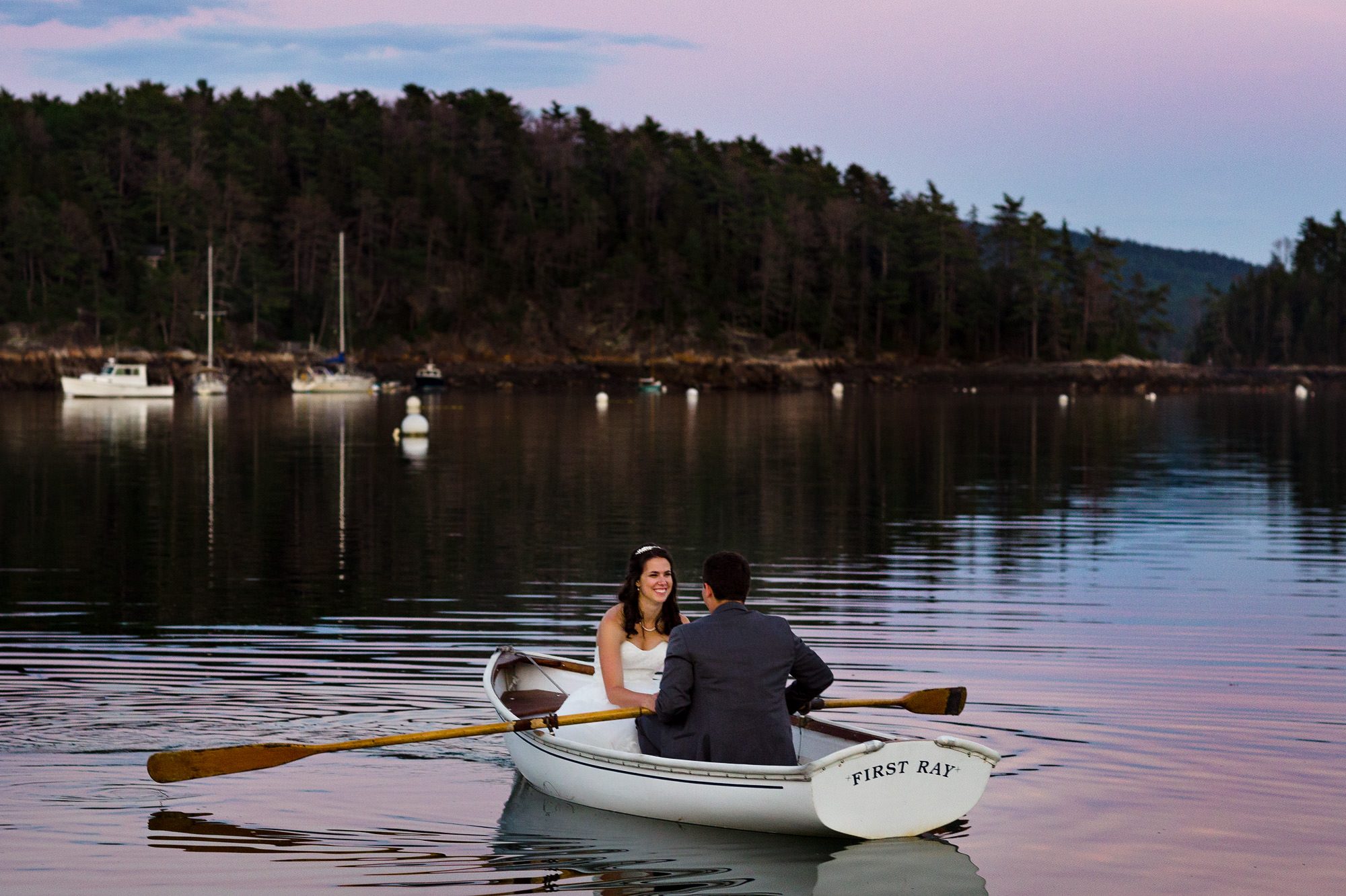 A bride and groom row in a rowboat at sunset at their coastal Maine wedding
