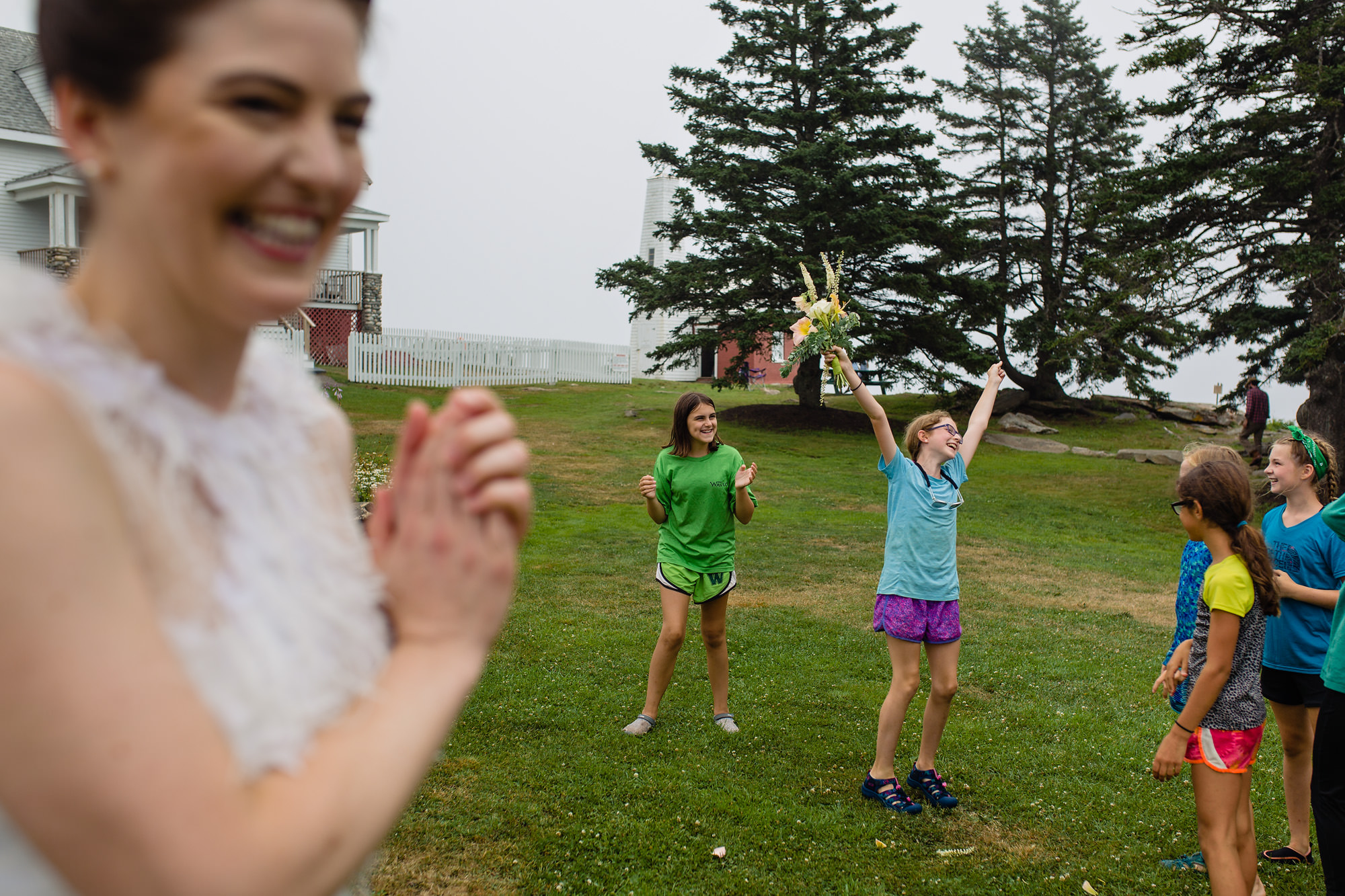 A bride throws her bouquet to a group of girls at a wedding at Pemaquid Point lighthouse in Maine