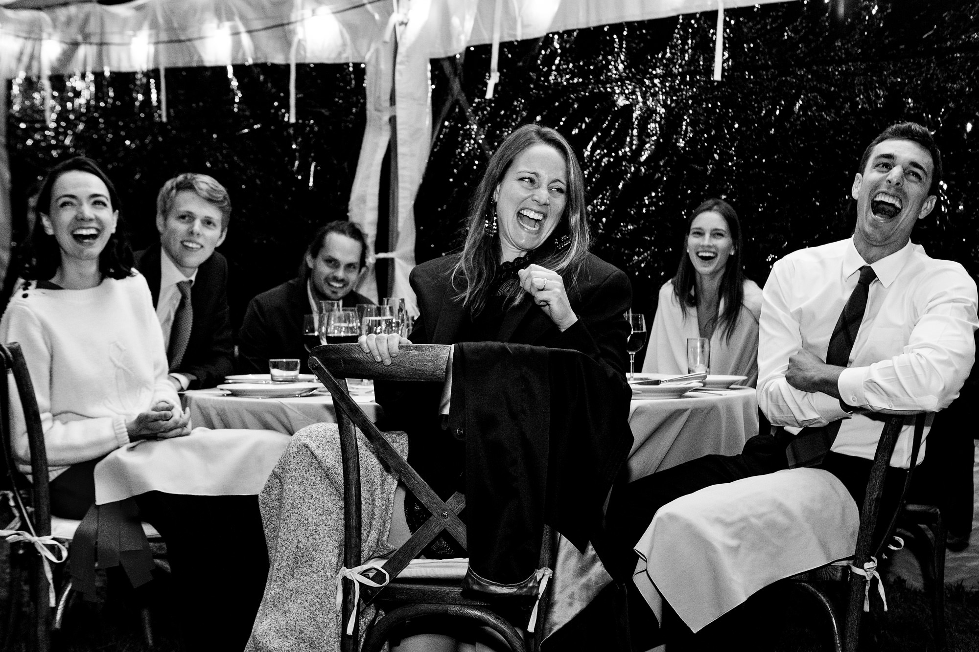 A table of friends laugh during a toast at a private residence Maine wedding