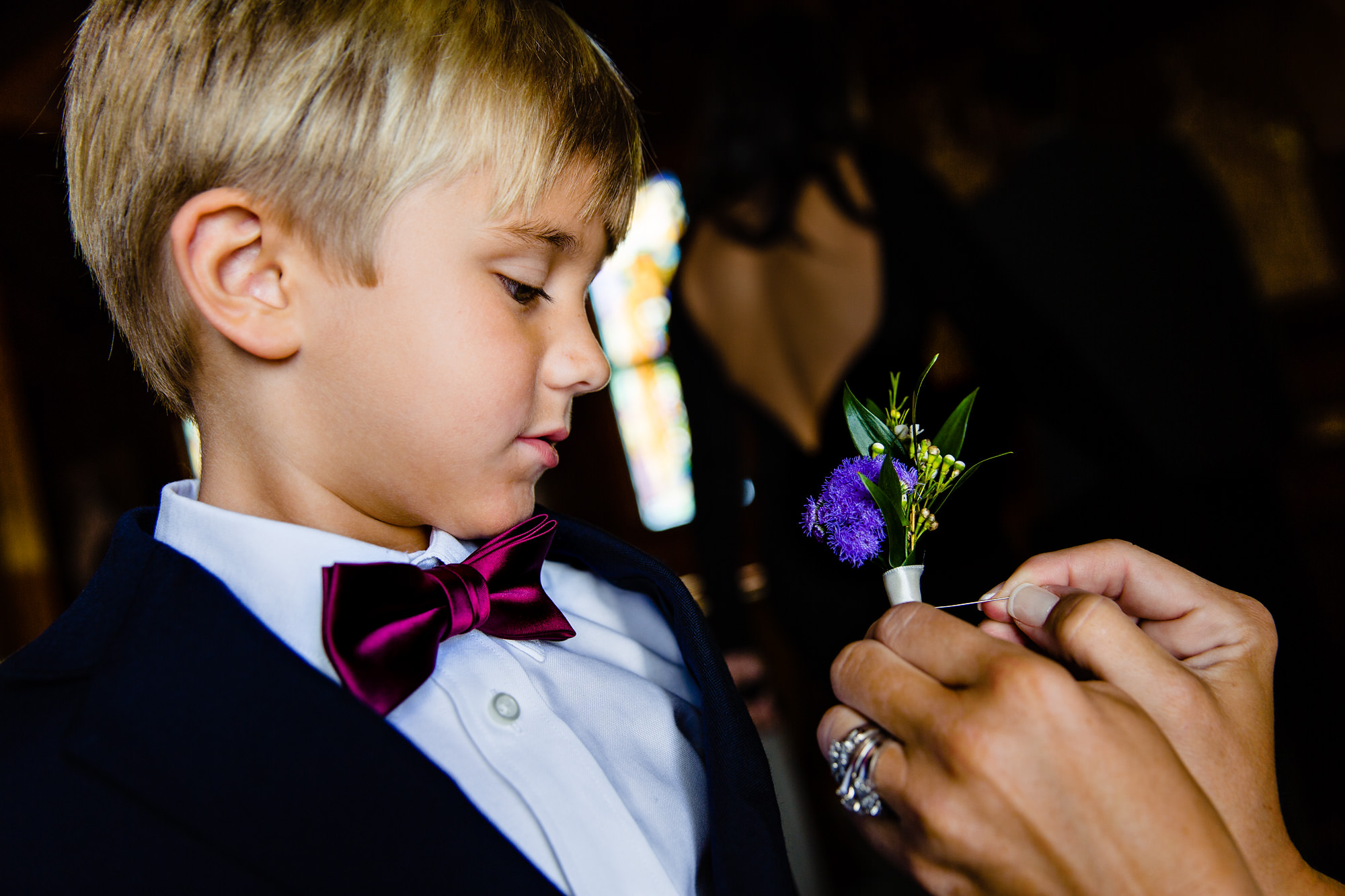 A ringbearer has a boutonniere pinned on him at Our Lady Queen of Peace in Boothbay Harbor, Maine