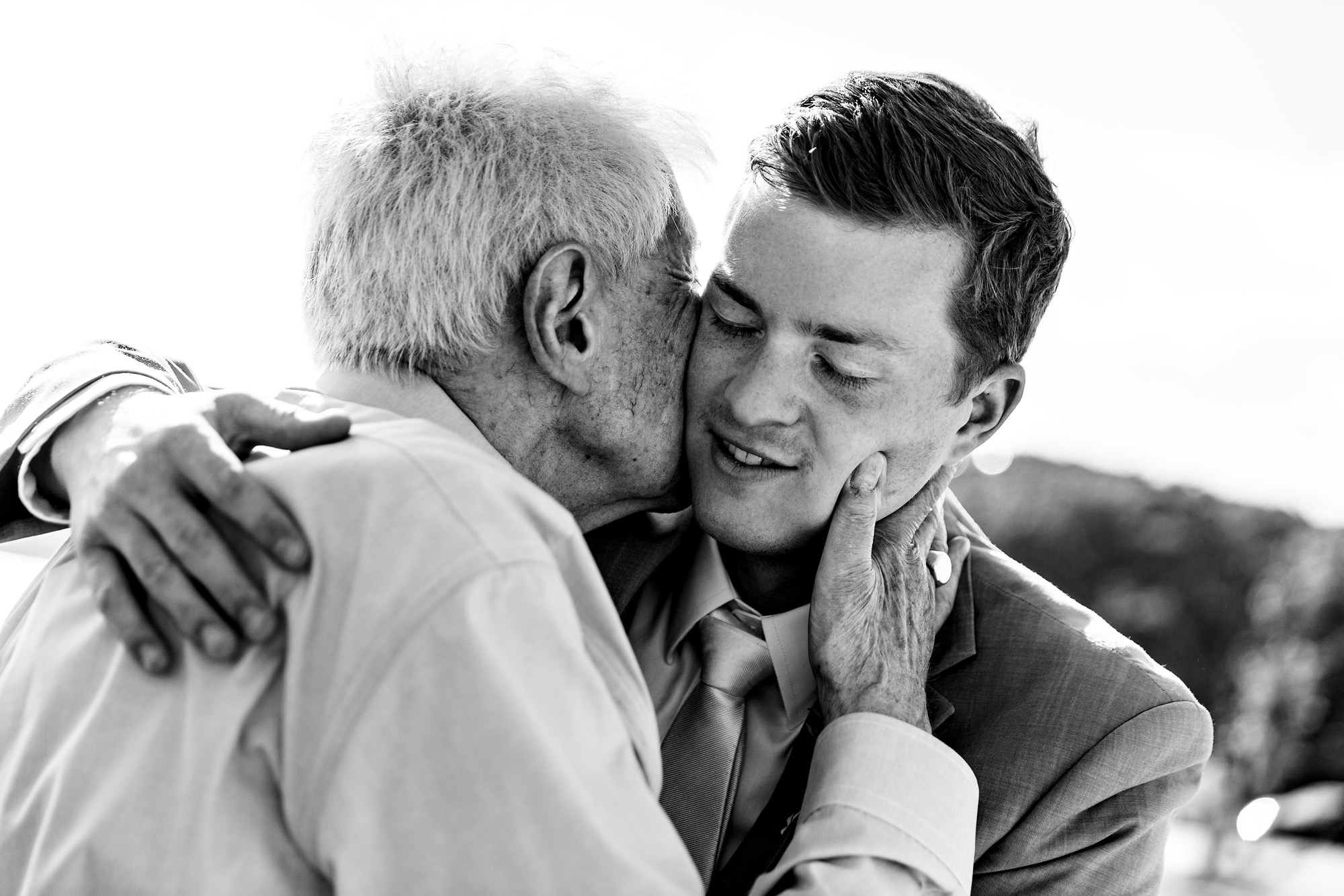 A grandfather kisses the groom on the cheek