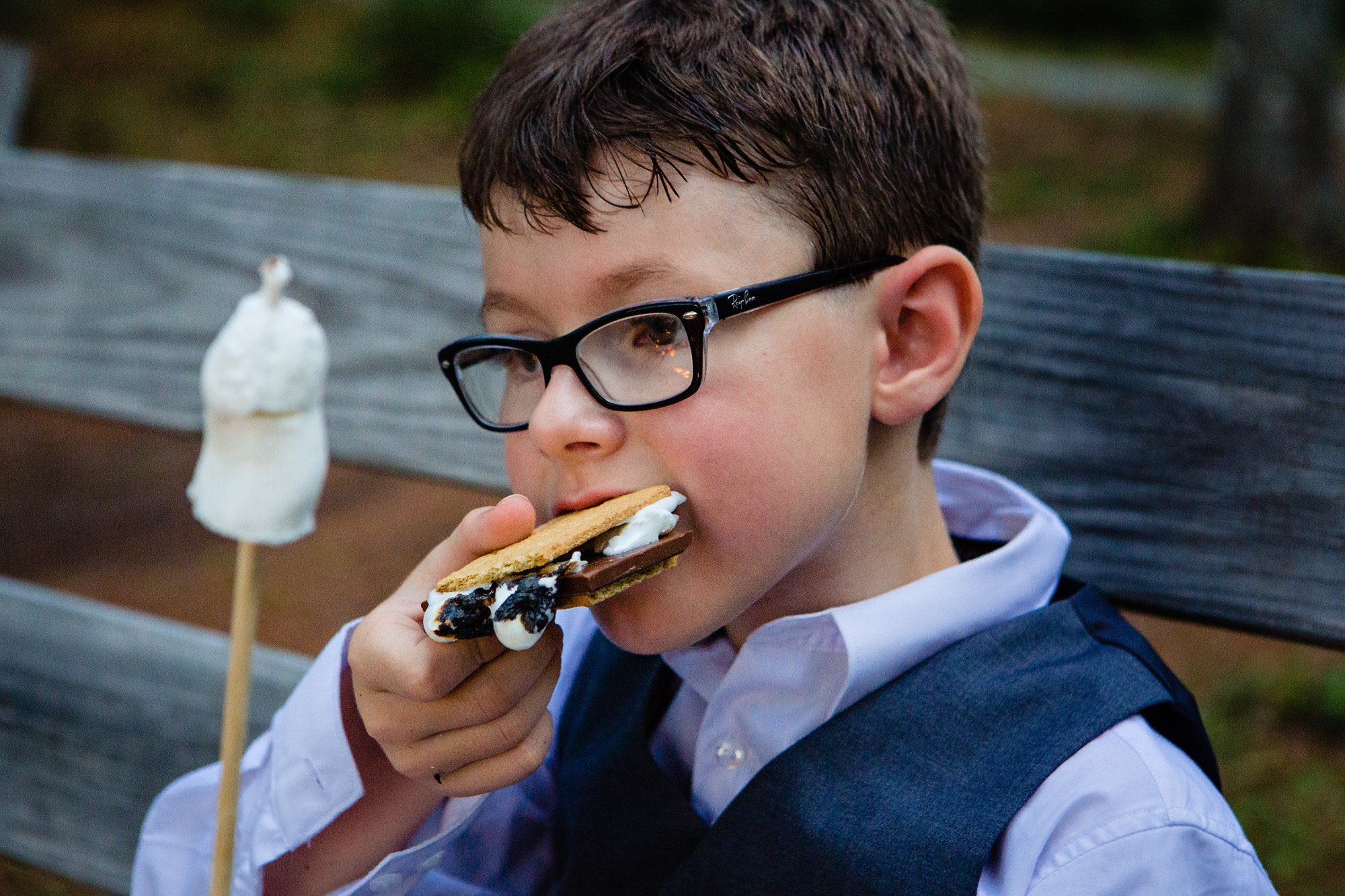 A kid stuffs a smore in his mouth at a lakeside wedding in Maine