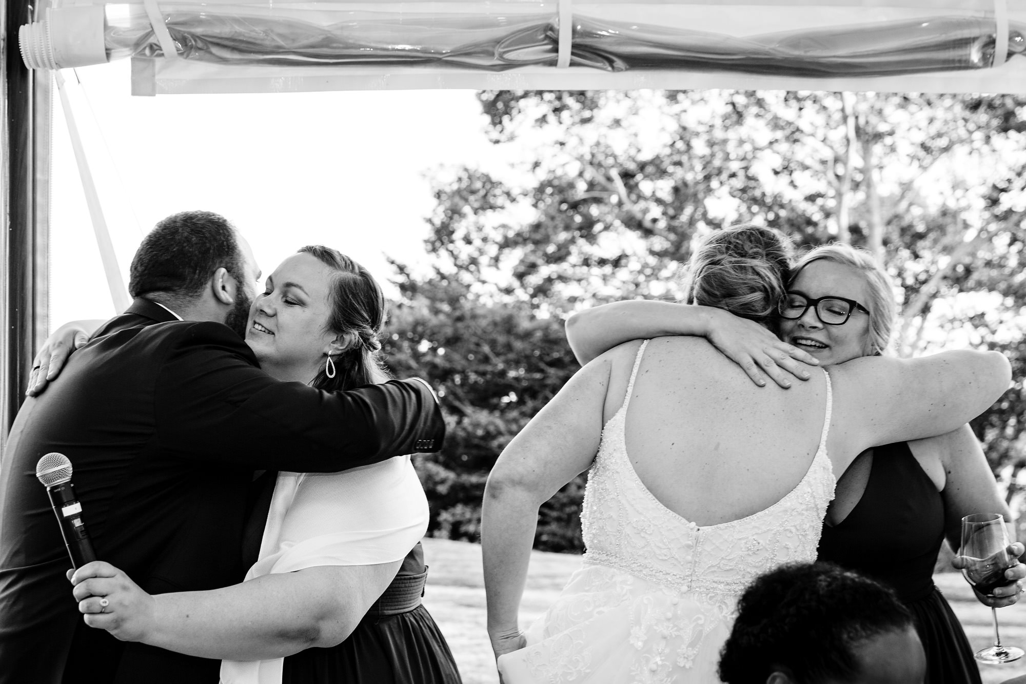 The bride and groom hug two bridesmaids after an emotional toast at their Maine wedding