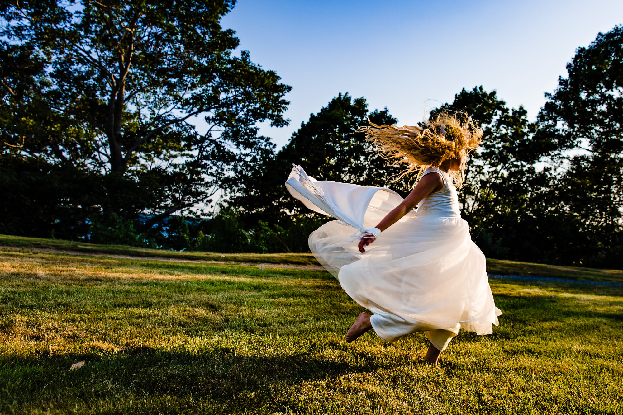 A flower girl frolics during golden hour at a wedding in Maine