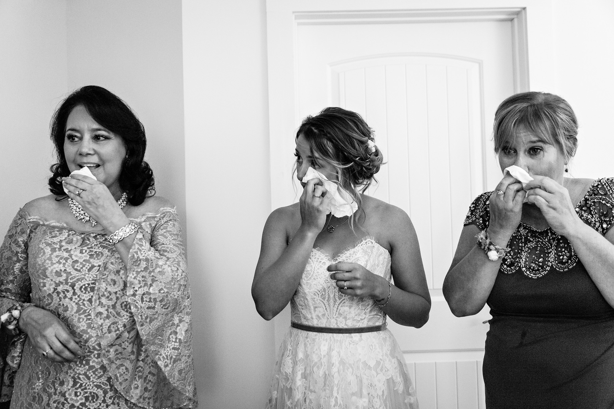 The bride holds her mother and her mother-in-law's hands as they pray and cry