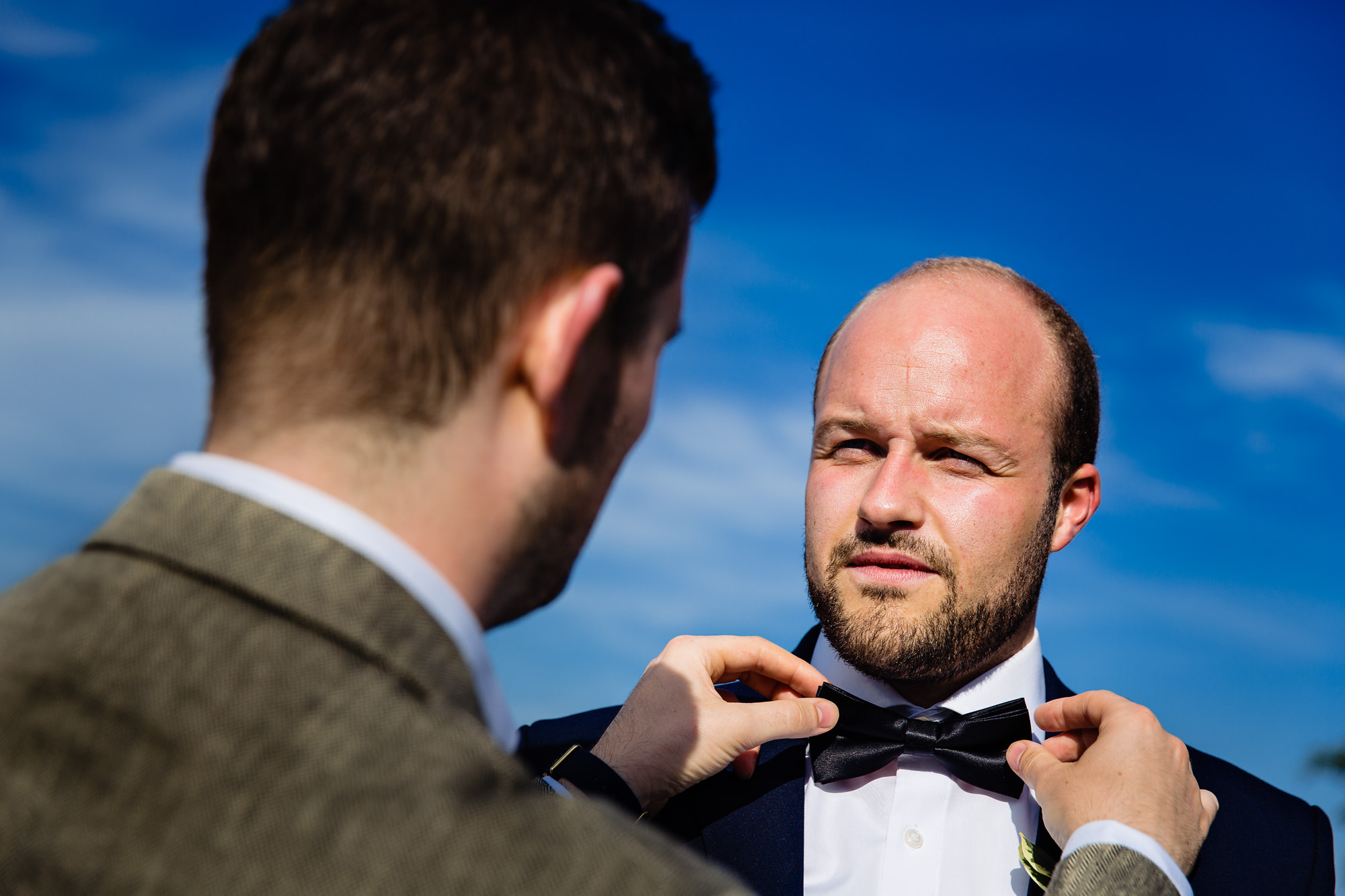 The groom perfects the best man's bow tie right before his wedding ceremony in Maine