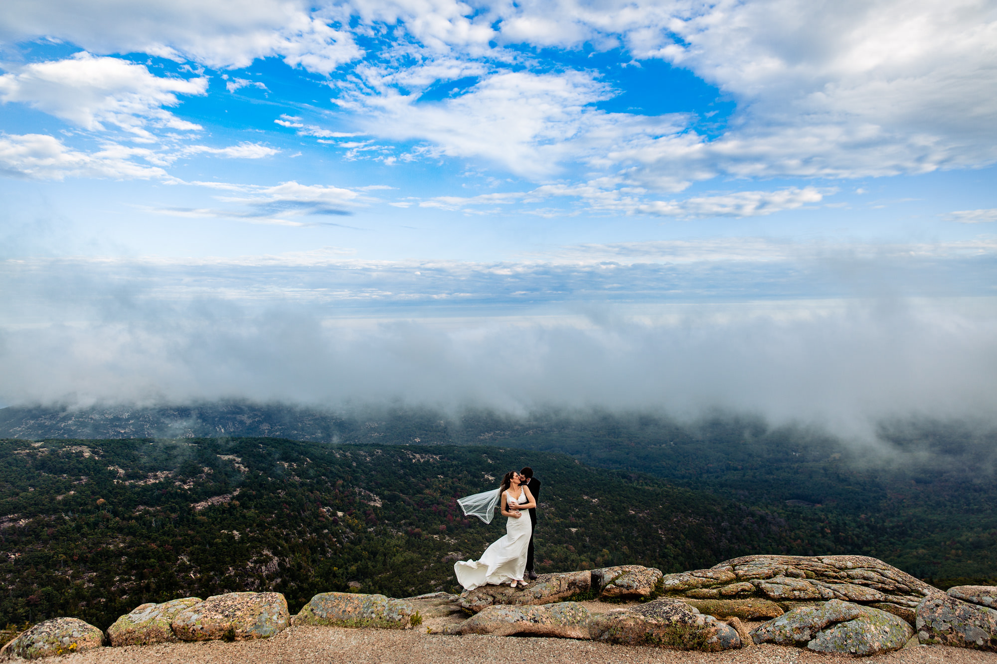 A bride and groom portrait on top of Cadillac Mountain on a windy day.