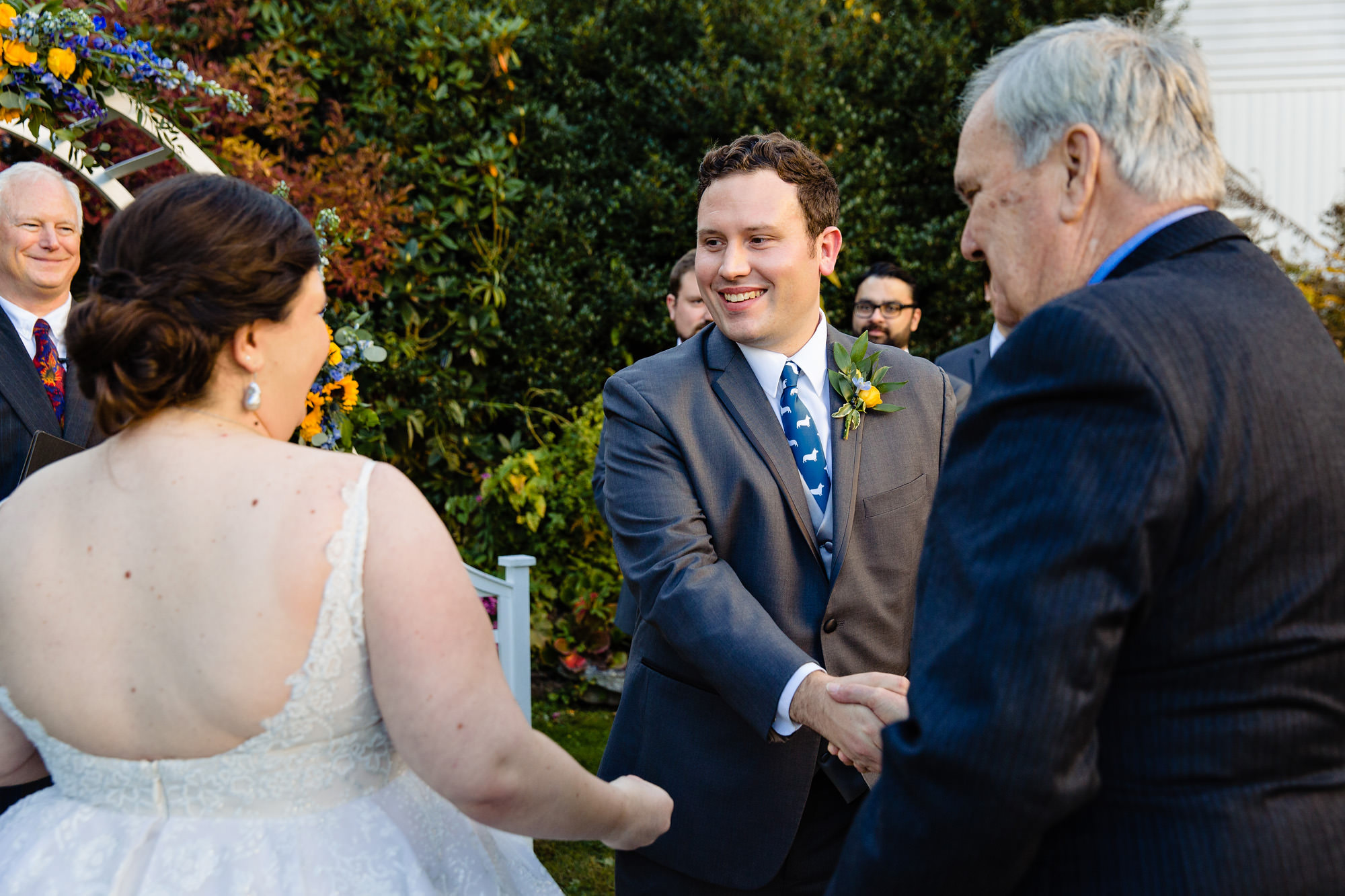 The groom shakes the father of the bride's hand while admiring the bride at their Freeport Maine wedding