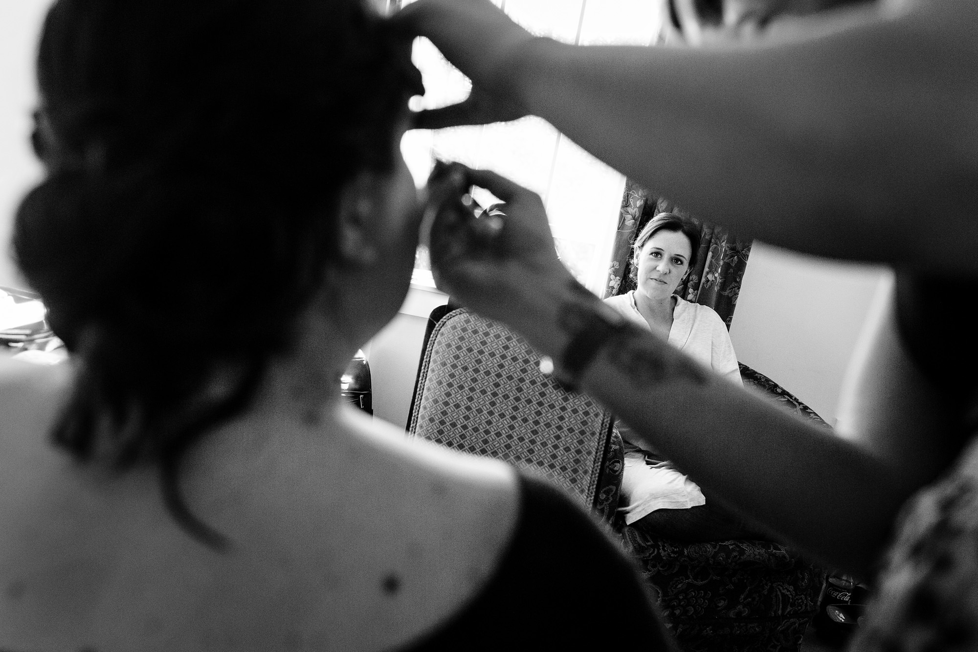 A bridesmaid watches as the bride has her makeup done at her Maine wedding