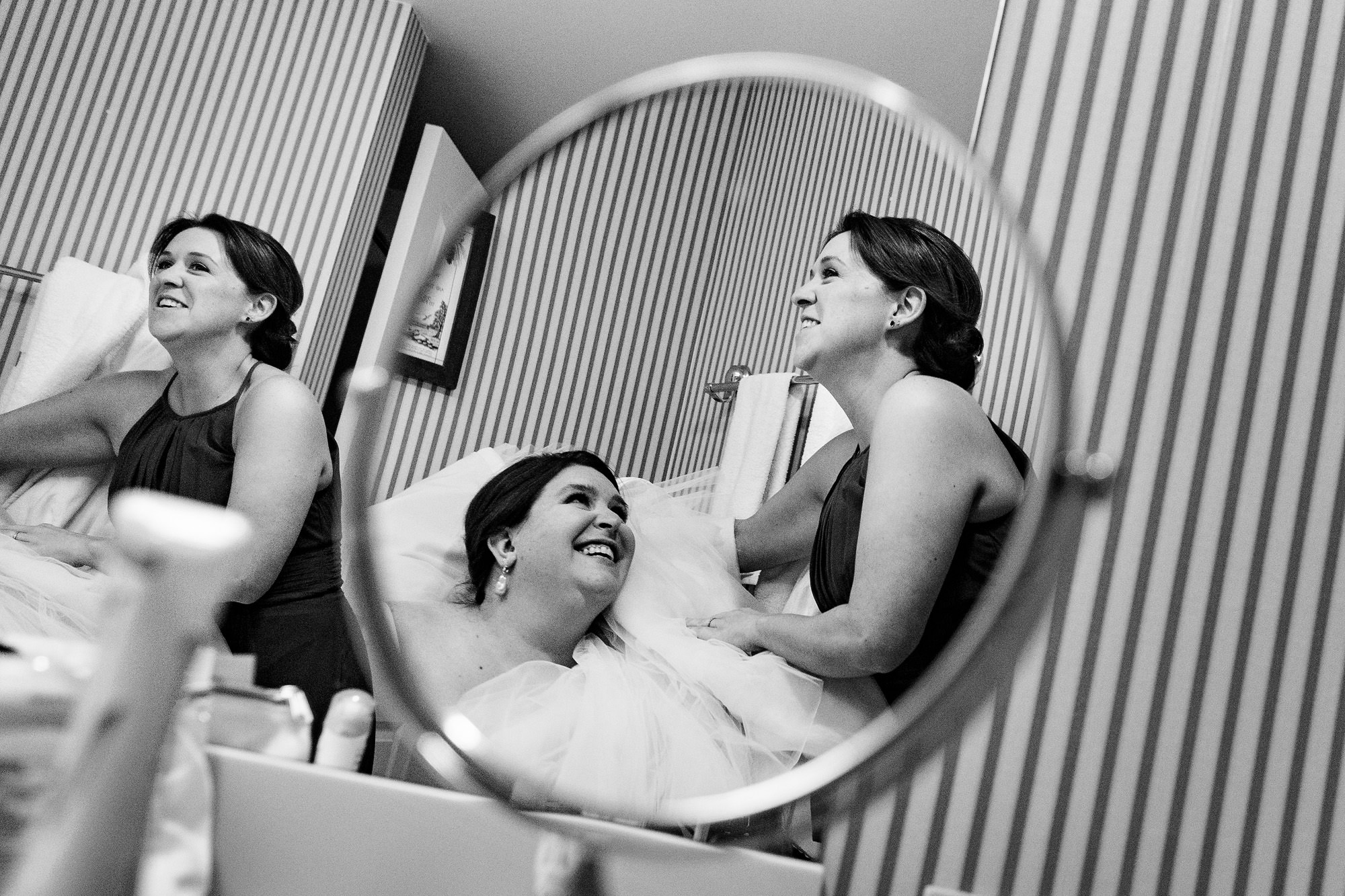 A bride laughs as she tries to use the bathroom while wearing her wedding dress