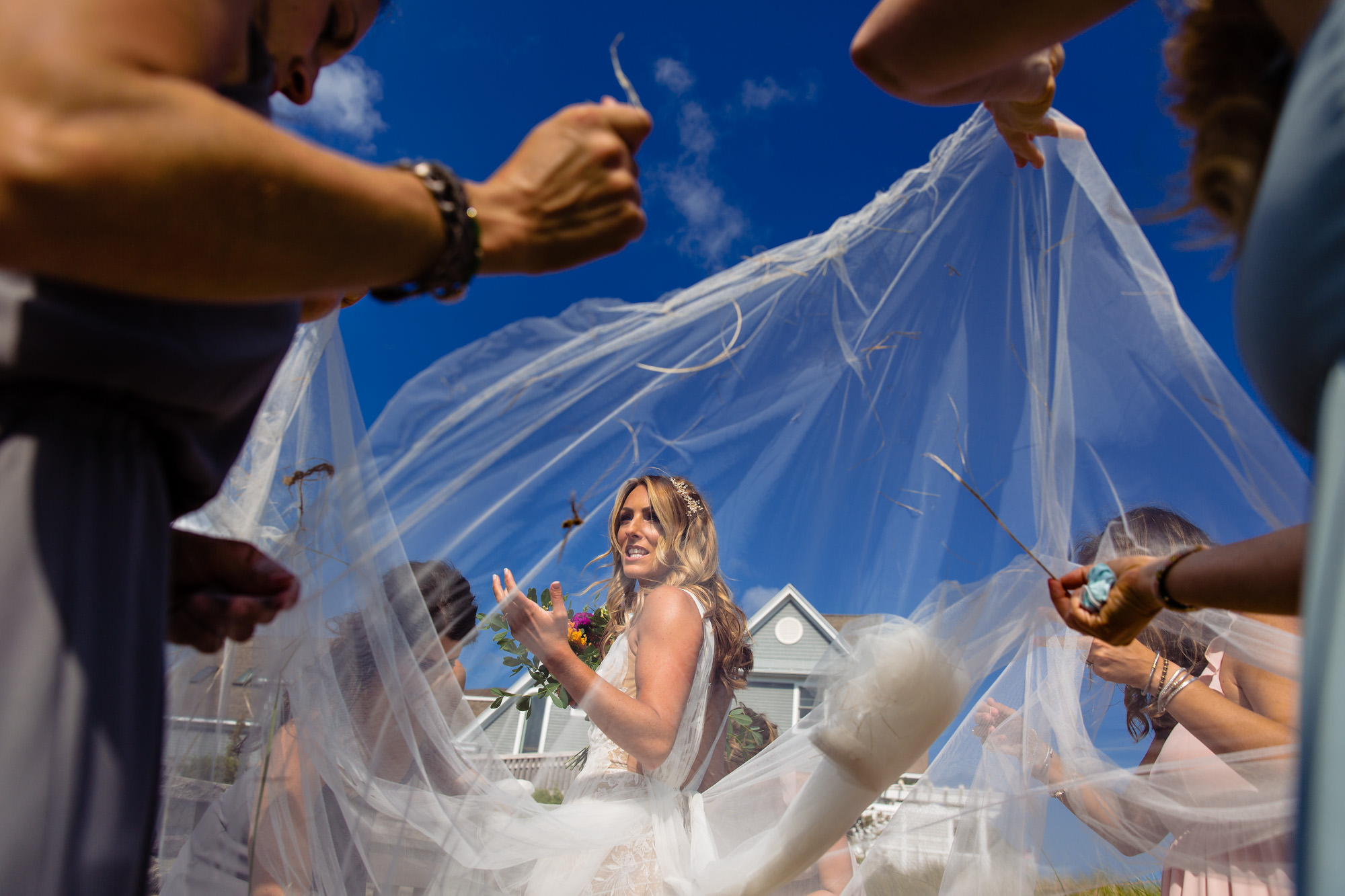 Bridesmaids pick sea grass out of the bride's dress at her southern Maine wedding