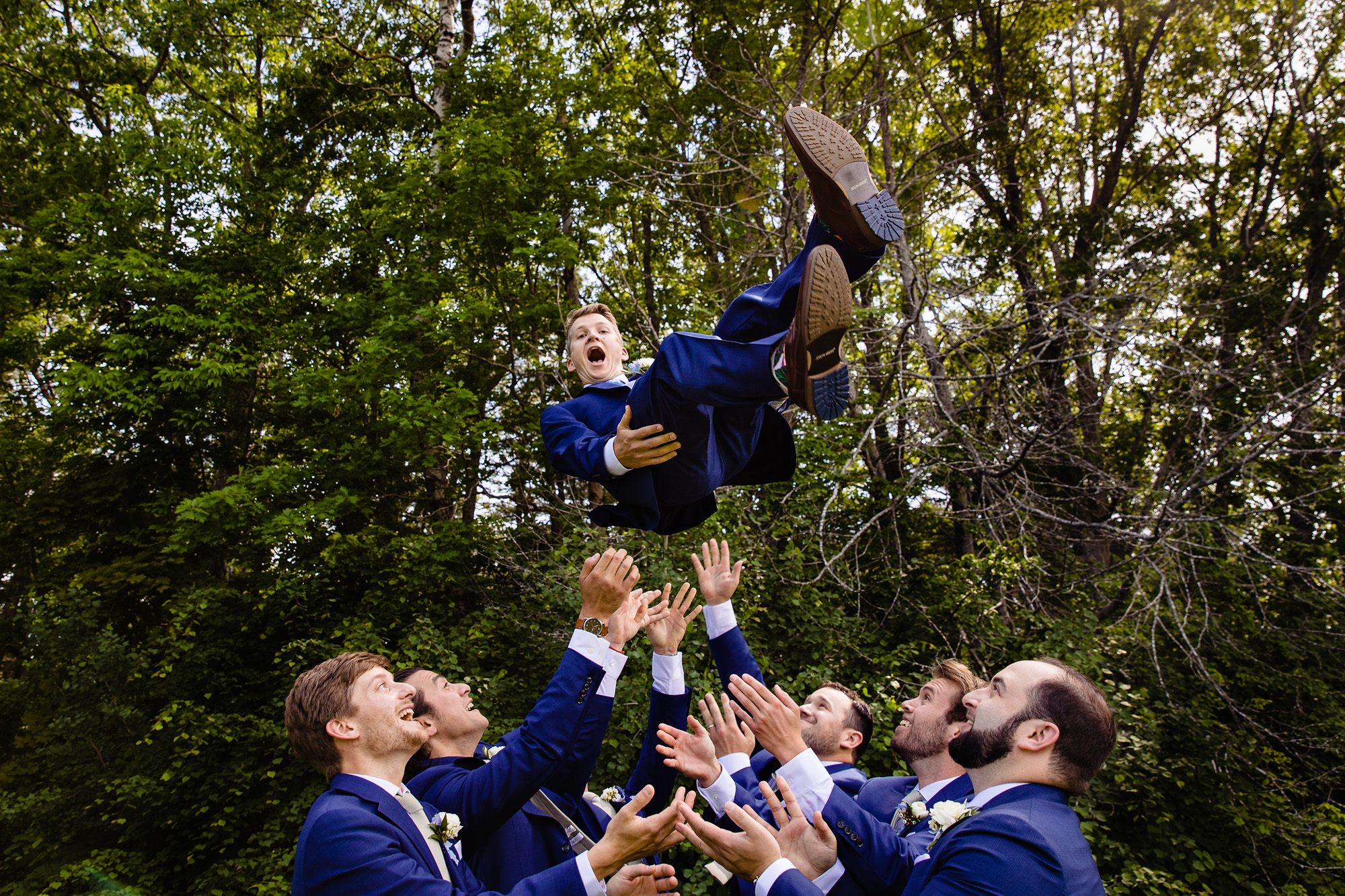 Groomsmen throw the groom into the air at his wedding at Marianmade Farm in Wiscasset Maine