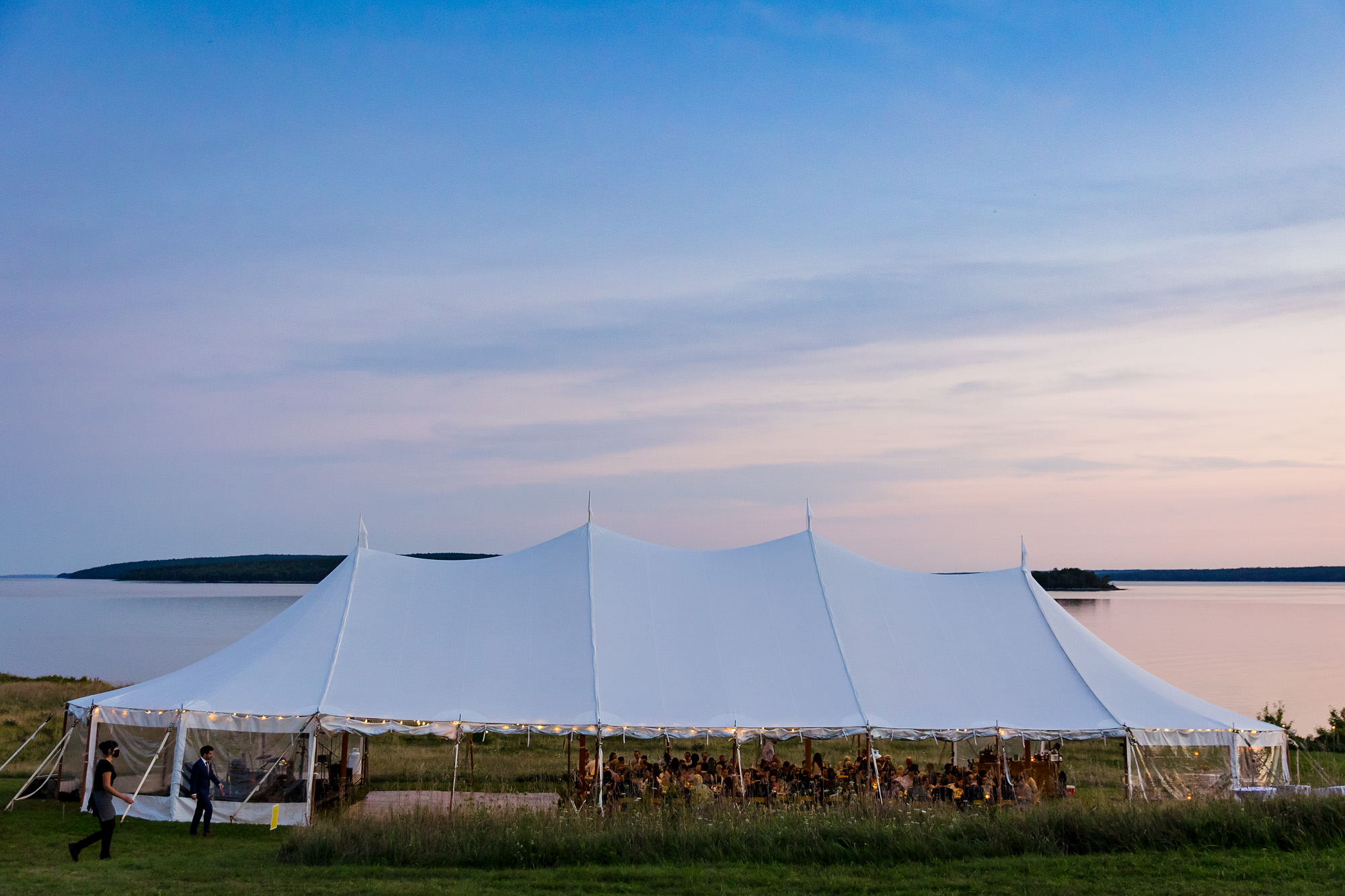 The sun sets behind a tented reception in mid coast Maine