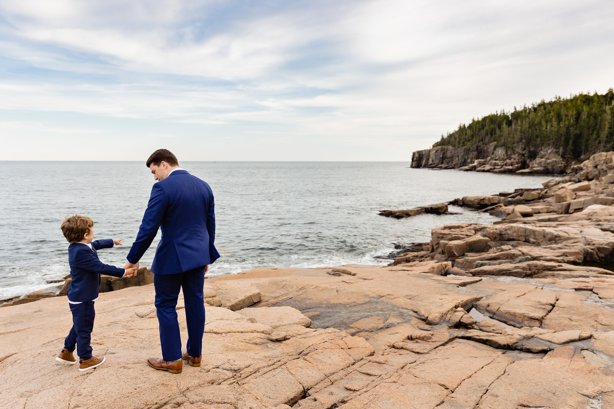 A groom walks with a boy along the cliffs in Acadia National Park