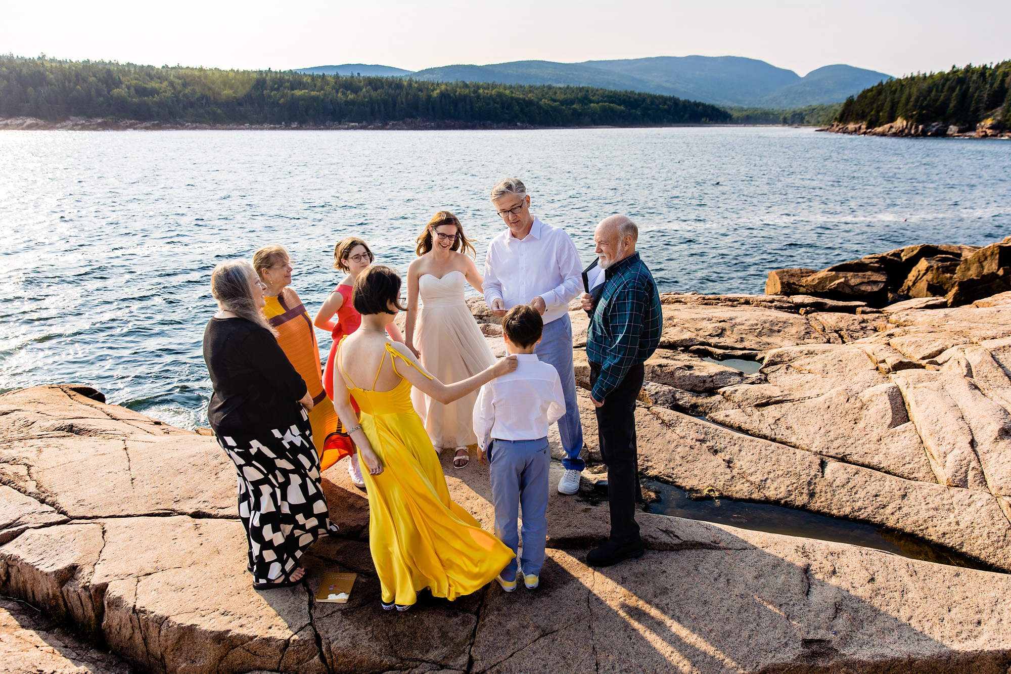 The wedding couple and their families stand in a circle for their Acadia cliffside elopement