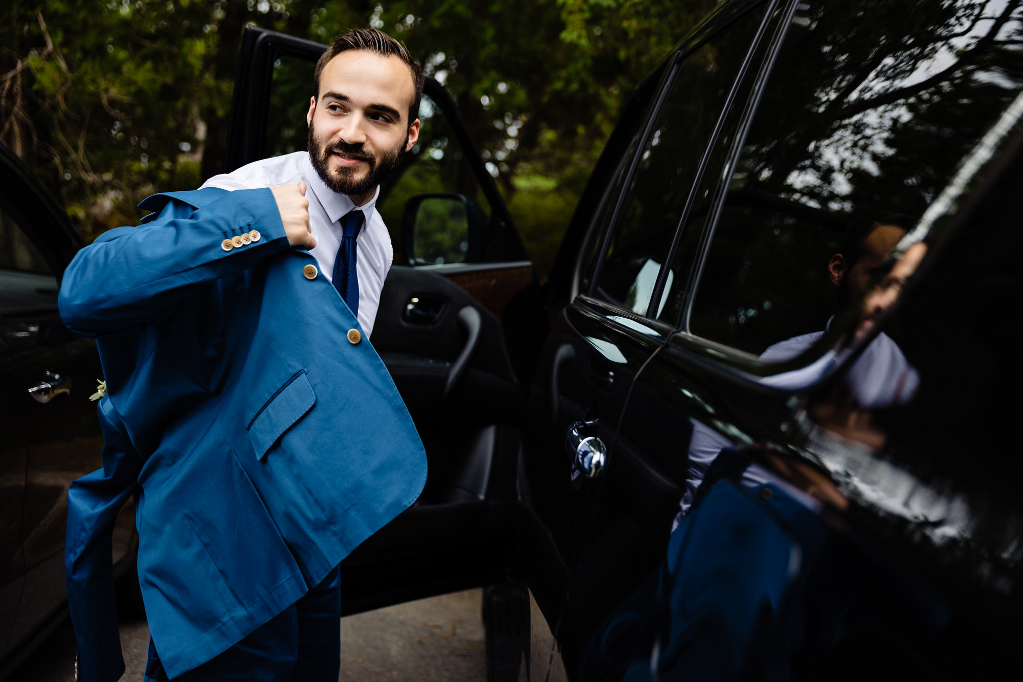 A groom puts on his jacket in an Acadia parking lot
