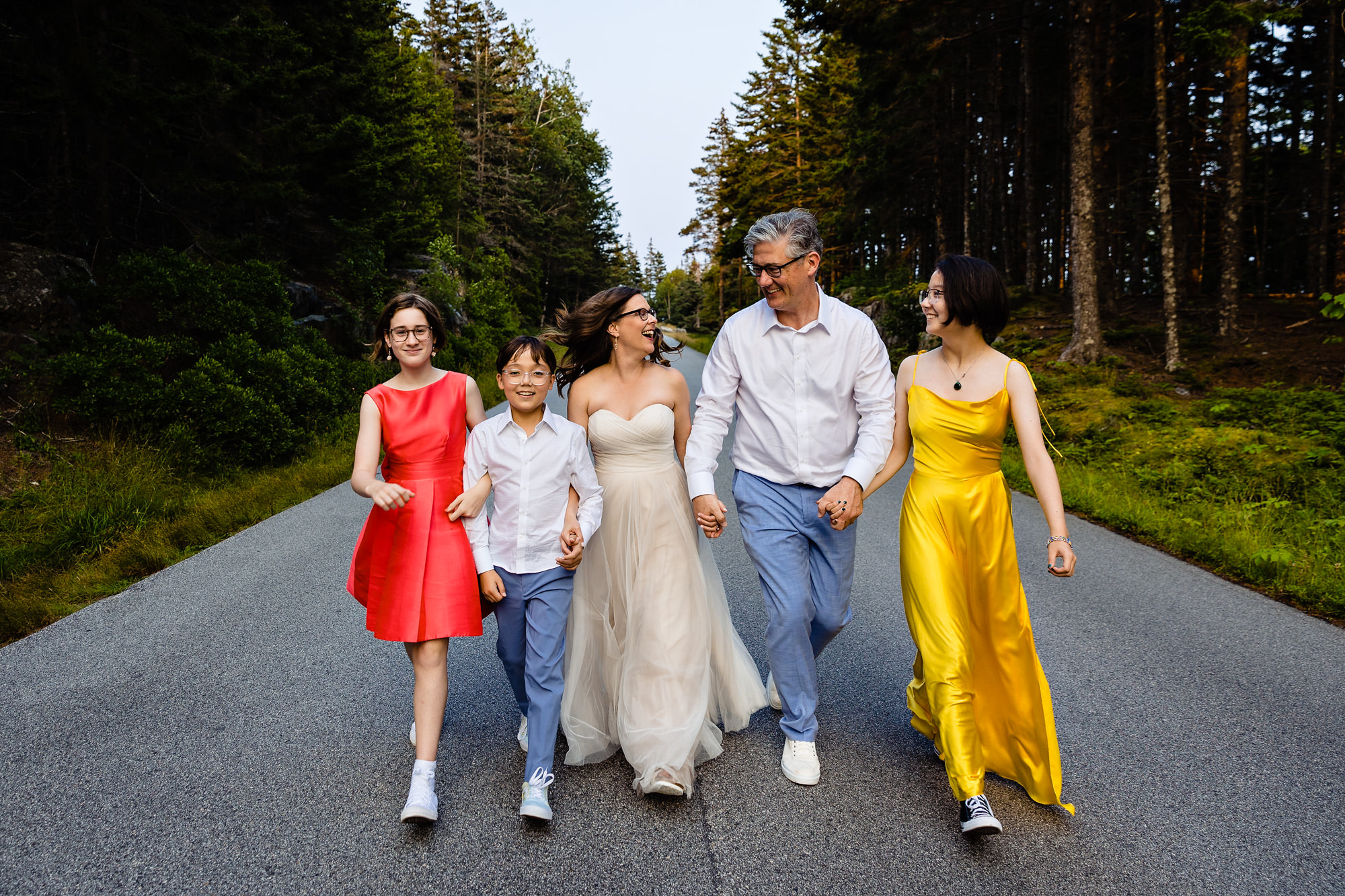 A family holds hands and walks down the park loop road in Acadia National Park during the couple's elopement
